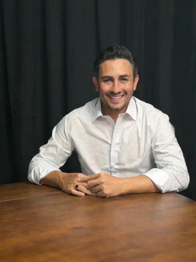 Ronaldo Ternus sentado à mesa, de camisa branca, sorrindo